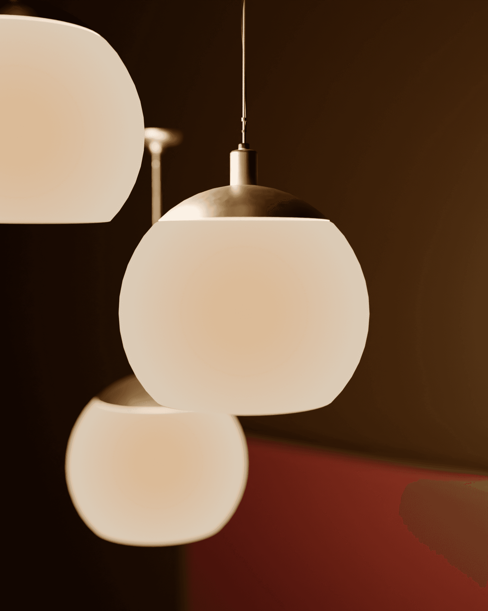 Close macro detail of two frosted glass globes and a brushed brass cap and stem, warm amber light glowing from within the glass, a garnet velvet banquette soft out of focus behind them